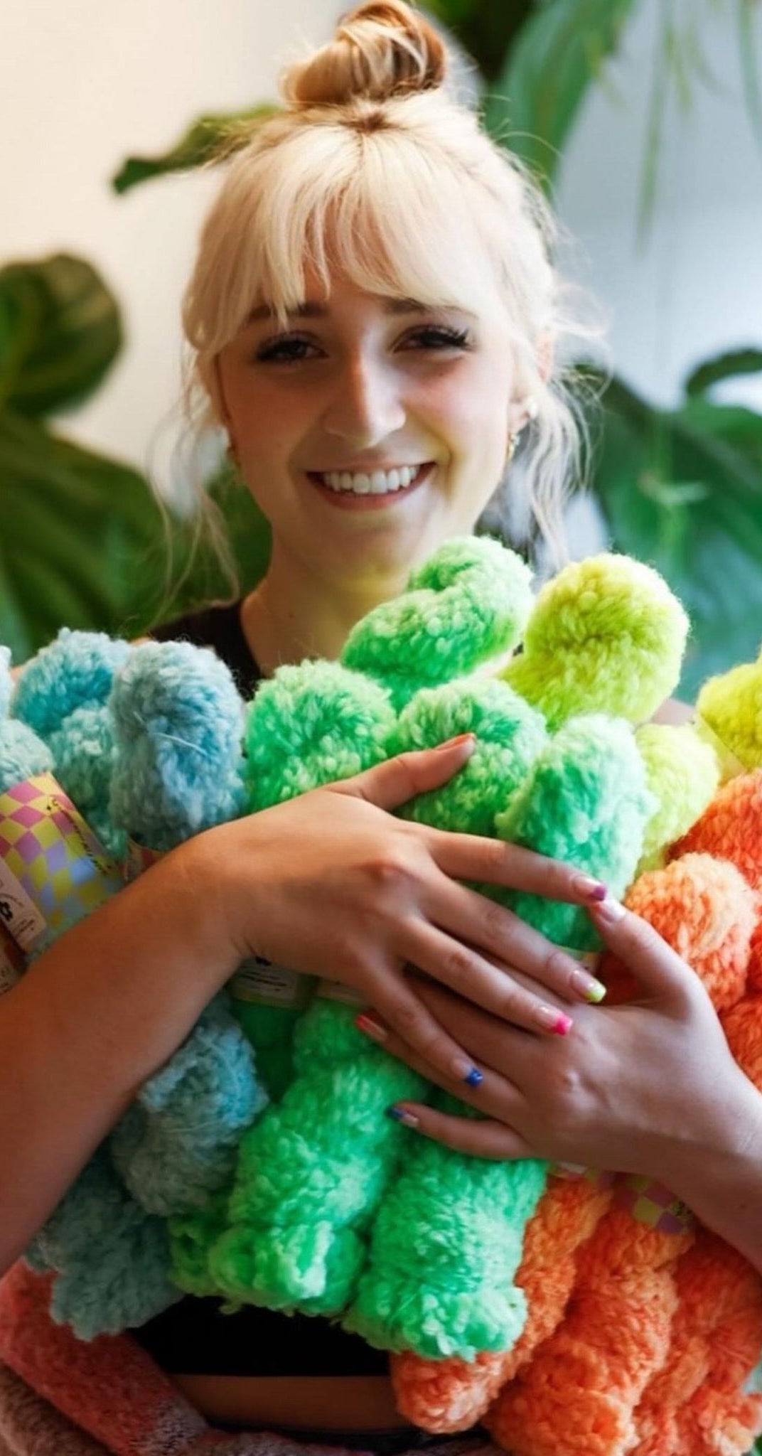 Person holding colorful yarn skeins with a blurred green plant background